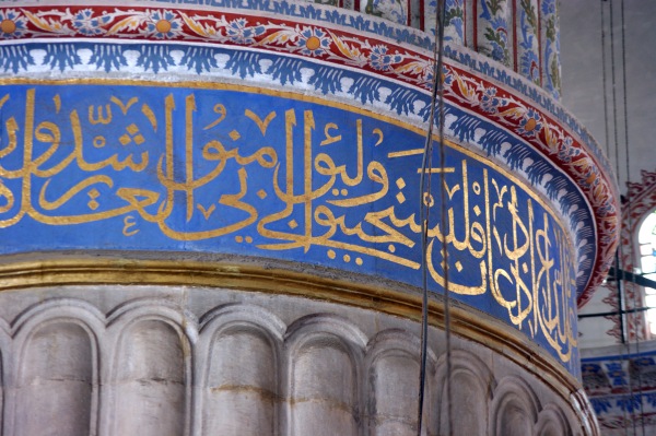 Arabic text from the Q'uran forms a frieze around the top of a massive main column