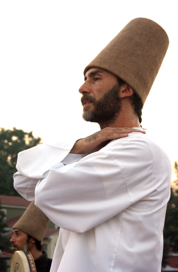 A dervish with a tall hat about to start dancing, arms clasped at his chest